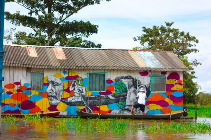 Apoiados em canoas, artistas criam mural de grafites em palafitas