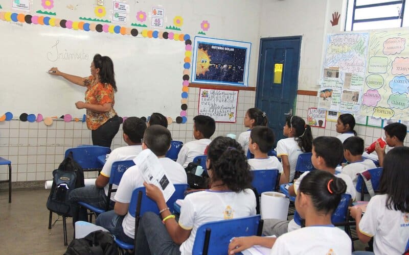 Professora em sala de aula ministrando conteúdo aos alunos.
