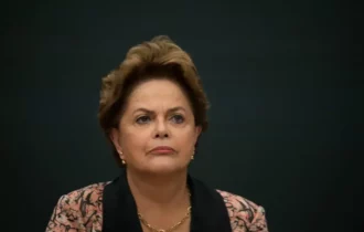 Imagem colorida mostra Dilma Rousseff séria com um fundo escuro