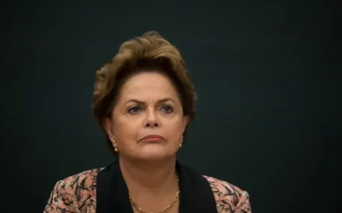 Imagem colorida mostra Dilma Rousseff séria com um fundo escuro